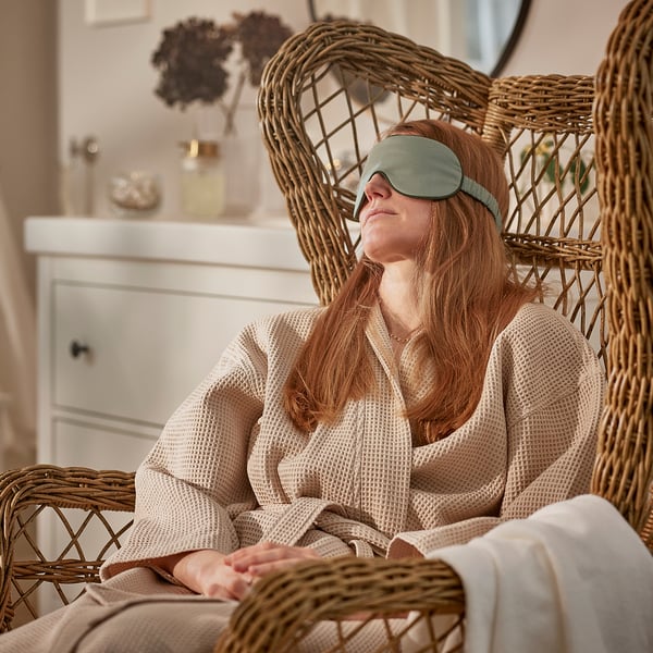 Person relaxing in wicker chair wearing green STJÄRNANEMON eye mask.