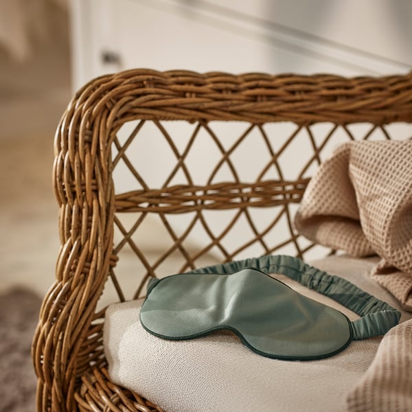 Green silk eye mask on wicker chair for relaxation.