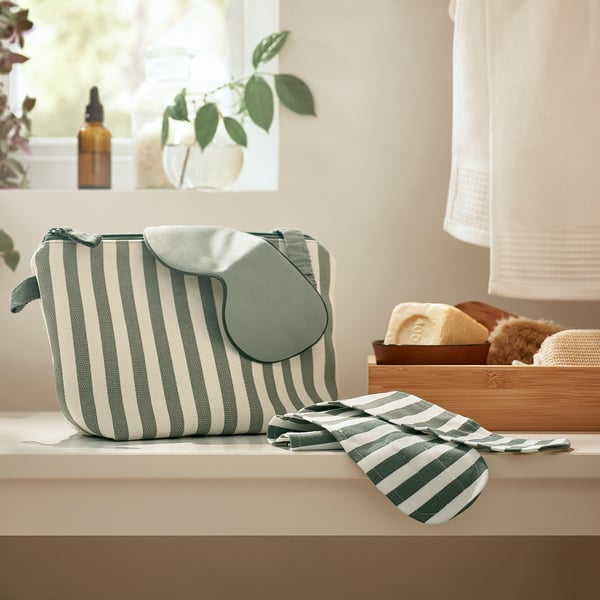 Green striped eye mask, soft cotton, curved shape, sits on counter by window.