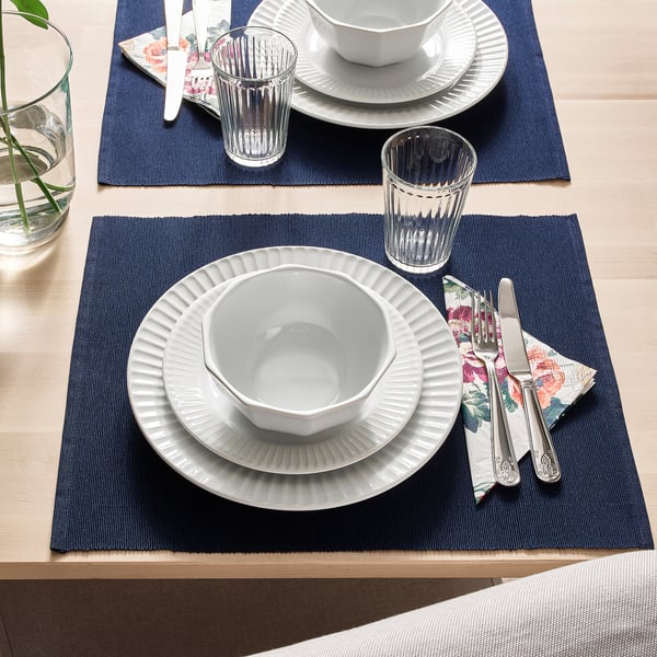 Table setting with STRIMMIG plates, bowls, glasses, and cutlery on dark blue mats. White porcelain with clean, modern details.