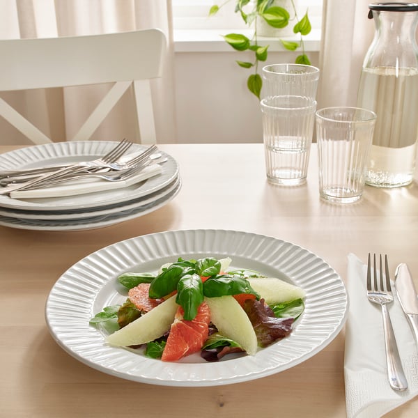 Table setting with white plates, cutlery, and glasses. Plate holds a colourful salad.