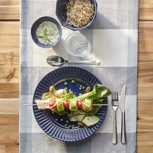A meal is served on a STRIMMIG blue plate, accompanied by side dishes and utensils on a chequered tablecloth.