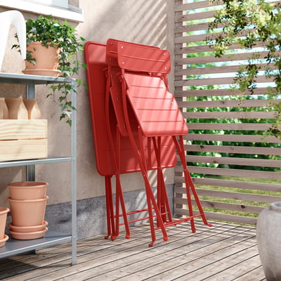 Bright red stackable metal chairs on wooden deck, leaning against wooden fence.
