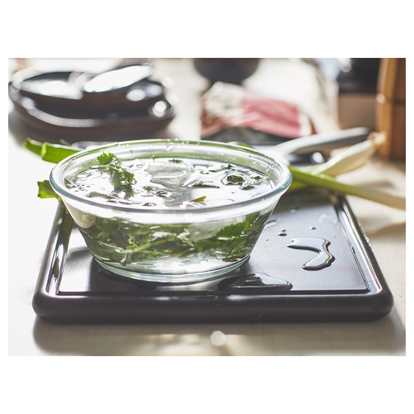 Clear bowl on black chopping board. Green herbs in water, scissors beside.