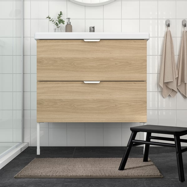 Modern bathroom with beige bath mat, vanity, black stool, grey tiles.