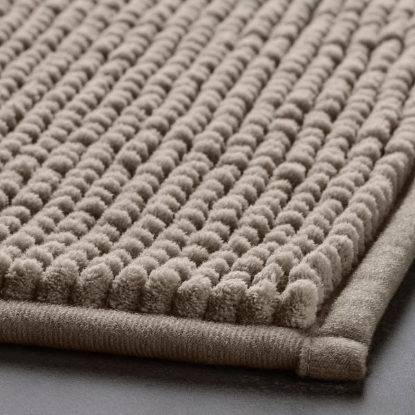 Close-up of a plush, textured grey bath mat with a raised diamond pattern for quick drying, made from recycled materials.