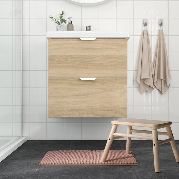 Modern bathroom with beige TOFTBO bath mat on dark tiles, light wood vanity, and matching towels.