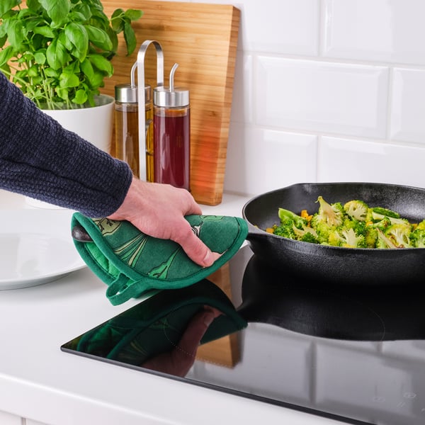 Cooking broccoli in skillet with green mitt.