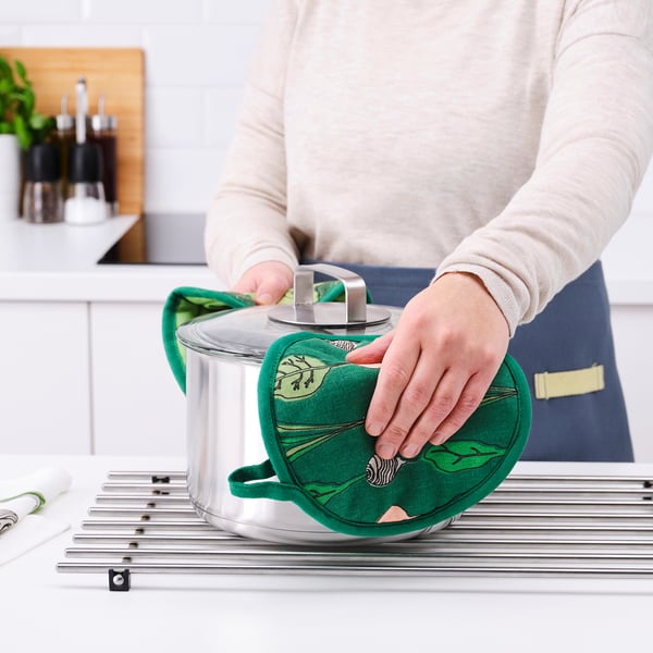 Person with green potholder in kitchen.
