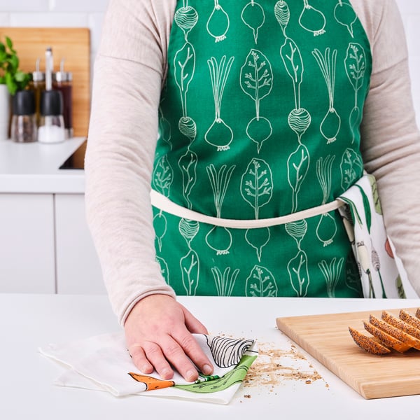 Person wearing green apron with vegetable patterns chopping food on a white counter.