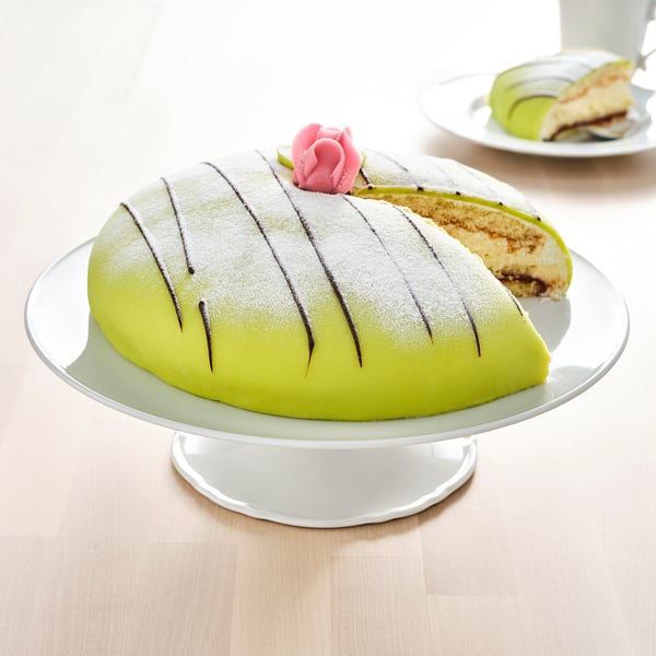 A bright green half-round cake on a white cake stand, dusted with icing sugar, showcased on a wooden table.