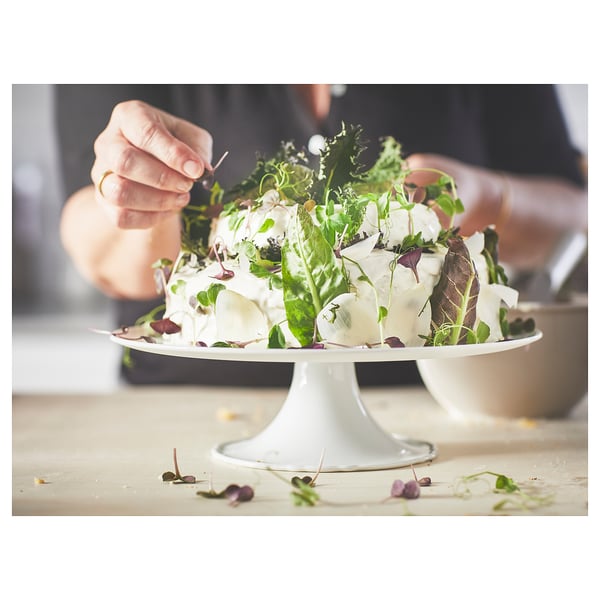 Hand decorating salad with greens on UPPLAGA cake stand, white porcelain with rustic design.