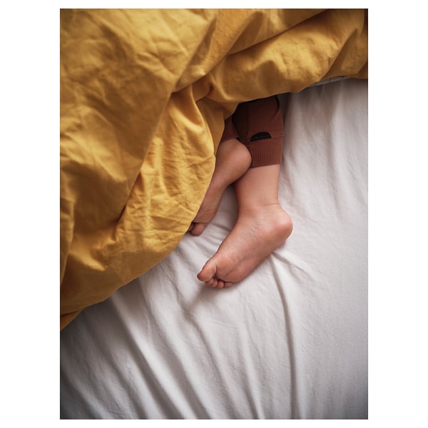 A childs feet under a yellow VÄNKRETS duvet cover, featuring a chequered and solid pattern, made of soft cotton.