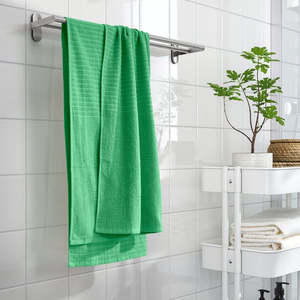 VÅGSJÖN green towel, soft cotton, hangs near plant, folded towels, white shelves, bright, clean tiles.