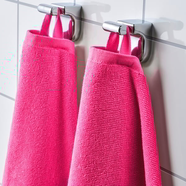 Bright pink towels hang from metallic hooks on white wall, neatly organised. Displays the towels vibrant colour and practical hanging system.