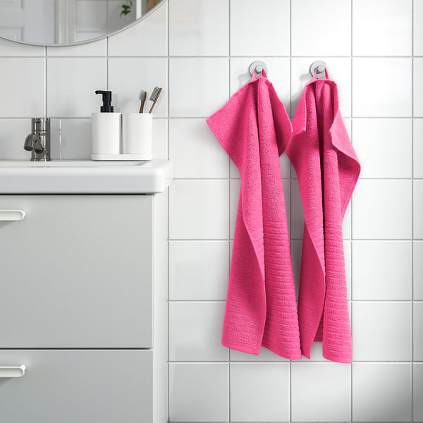 Pink VÅGSJÖN towels hang on silver hooks by sink, adding vibrant colour to minimalist bathroom.