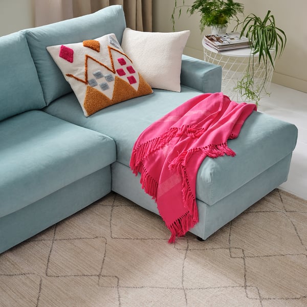 Light blue VIMLE sofa with pink throw blanket and decorative pillows. Modern design with beige patterned rug. Placed near a plant.