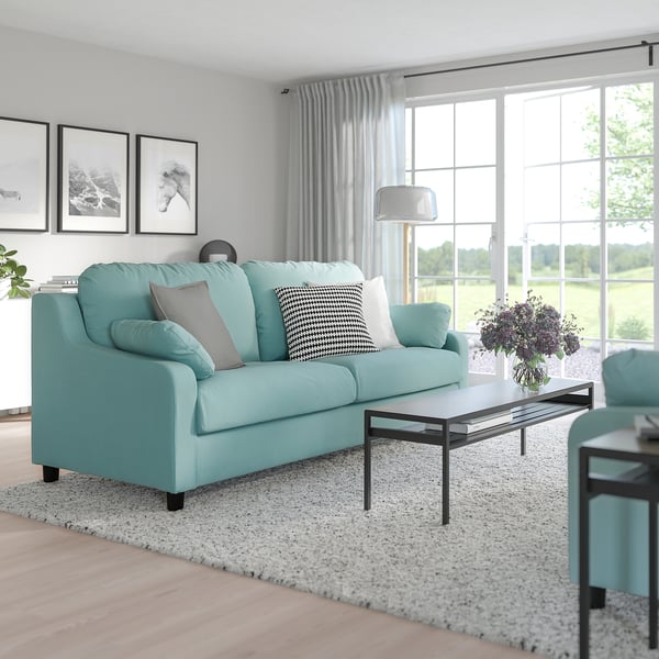 Modern living room VINLIDEN light blue sofa, large cushions, black coffee table, and wall art. Sofas size complements big windows, curtains, and rug.