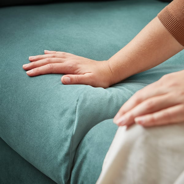 Two hands gently resting on a soft, light blue, textured cushioned surface. The focus is on comfort and support, likely from a VINLIDEN sofa.