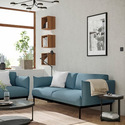 Modern living room with blue ÄPPLARYD sofa, wooden shelves, and a black-framed photo.