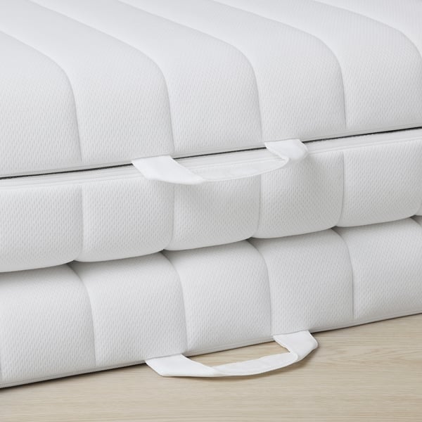 Close-up of firm, white mattress with ridged pattern, showcasing intricate stitching and folding design, ensuring comfort and support.