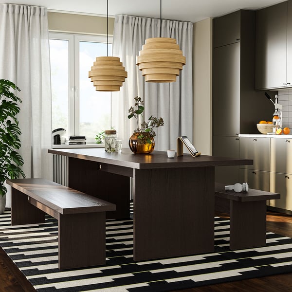 Modern kitchen with dark wood island and pendant lights. Bright rug, plants, and large windows.
