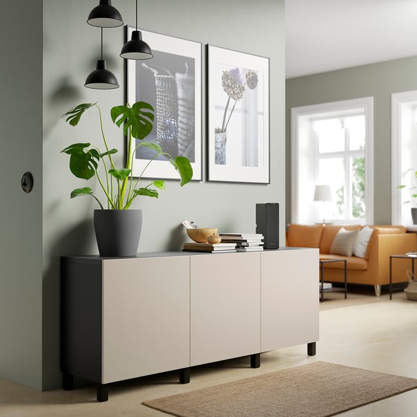 White & black BESTÅ sideboard with adjustable shelves & modern design. Against a wall, between framed pictures & hanging lamps.
