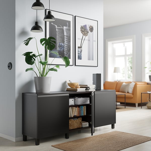 Modern living room with black BESTÅ sideboard, potted plant, books, and orange sofa. Two framed pictures hang above.