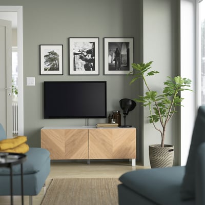 Modern living room with BESTÅ tv stand, blue couch, yellow pillow, black lamp, photos, and green plant in basket.
