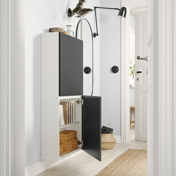 Modern, wall-mounted white BESTÅ storage unit with grey doors. Black handles and an adjustable light fixture.