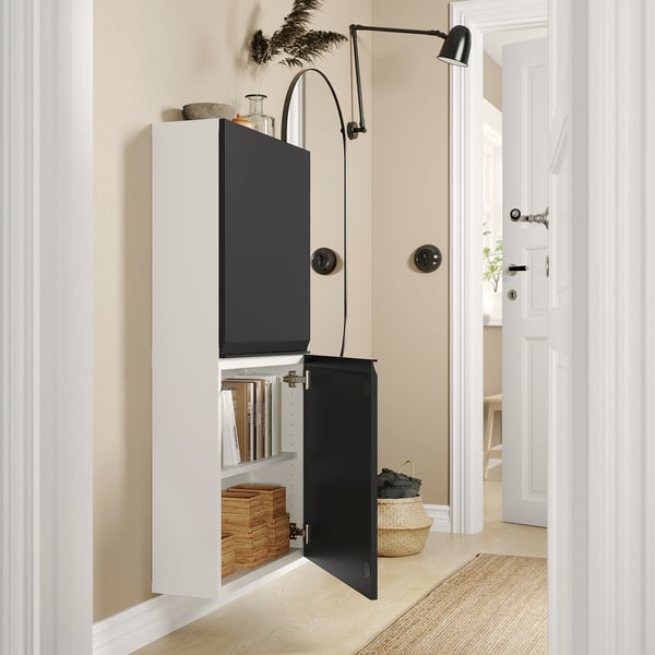 Modern storage solution: BESTÅ cabinets in black and white, sleek design, wall-mounted, open door revealing books and bins.