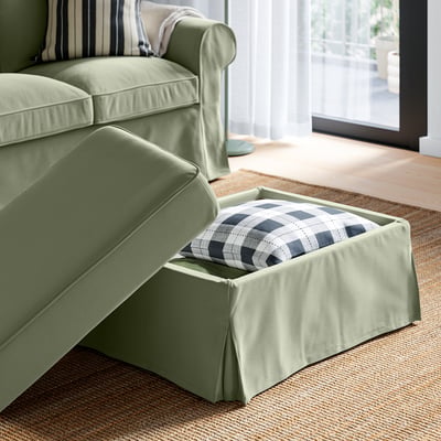 Green EKTORP footstool, with open storage space showing chequered cushion, designed for easy organisation and comfort.