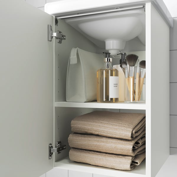 Open bathroom cabinet with towels, soap dispenser, and makeup brushes.