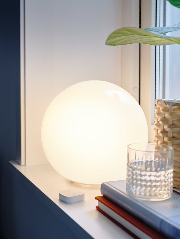 Small round white lamp on a shelf, with a remote and books beside. Soft glow, modern design.