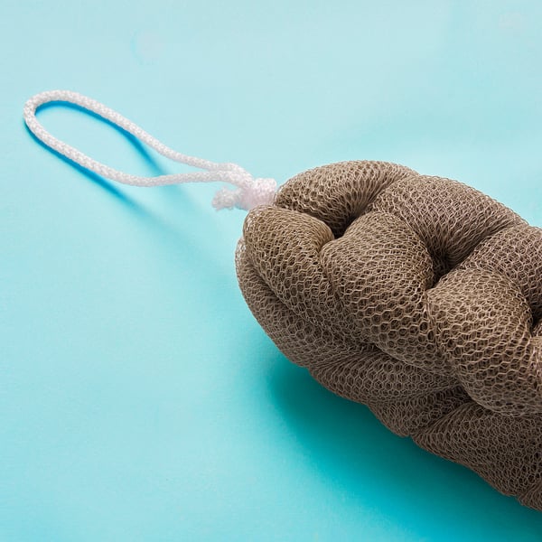 A brown bath sponge with a white rope handle sits on a blue background.