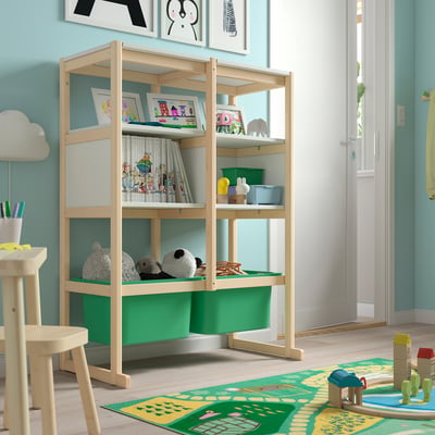 A light wood-colored FLISAT storage unit with shelves holding books and toys. It stands near a door and has green plastic bins at the bottom.