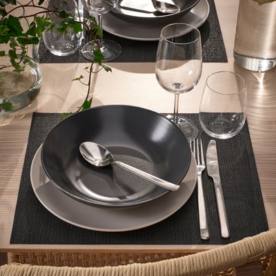 Table set with FLYGFISK place mats, black and grey dishes, cutlery, and glasses.