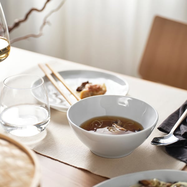 White bowl of noodle soup on table, with glasses, chopsticks, and napkin.