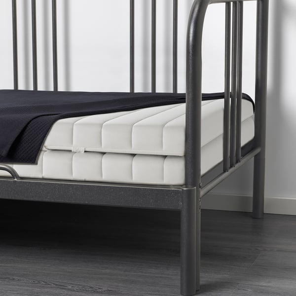 A corner of a black metal day-bed frame with white mattress, demonstrating its transforming functionality for guest accommodation or relaxation.