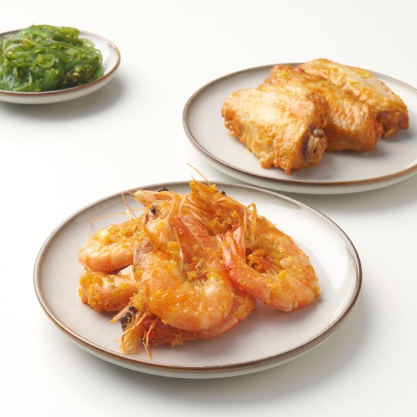 Three white plates with brown rims display cooked shrimp, fish, and greens.