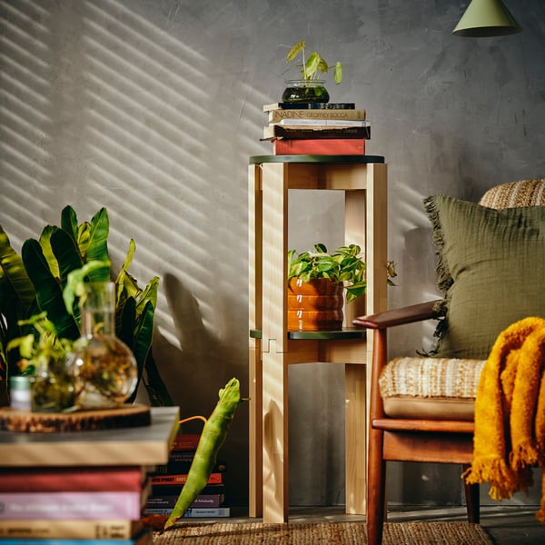 A stylish wooden plant stand made of stackable birch stools displays books, plants, and cushions.