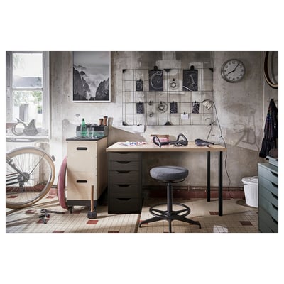 Industrial-style workspace with LAGKAPTEN desk, black drawers, wooden top, bike decor, and hanging clock.