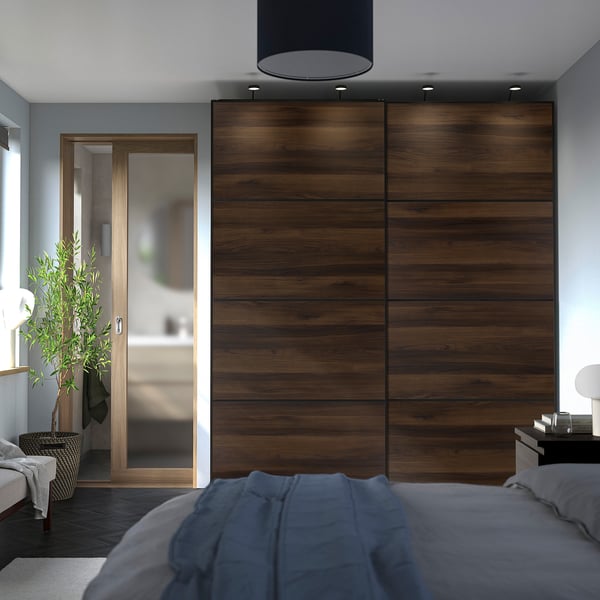 Dark wood closet doors, modern bed with grey sheets, plant by mirrored door.