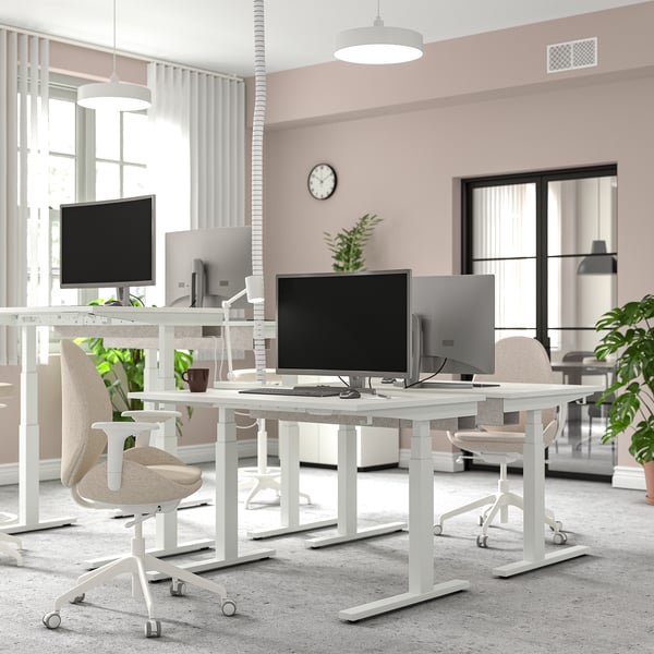 Modern office with MITTZON white desks and chairs. Spacious design, large monitors, plants, and clocks.