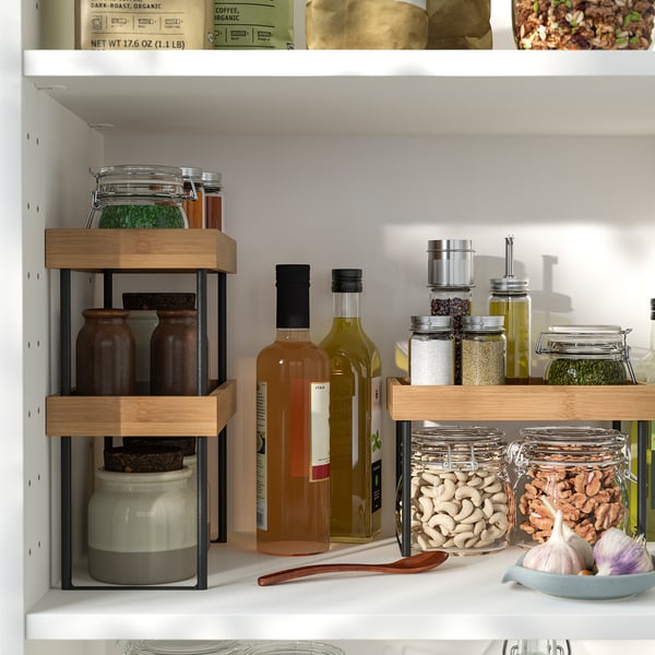Well-organized kitchen shelf with NÅLBLECKA bamboo storage. Jars and bottles neatly stacked on tiered stands.