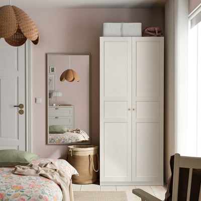 Cosy bedroom with white PAX wardrobe, floral bedding, hanging wicker basket, and beige rug.