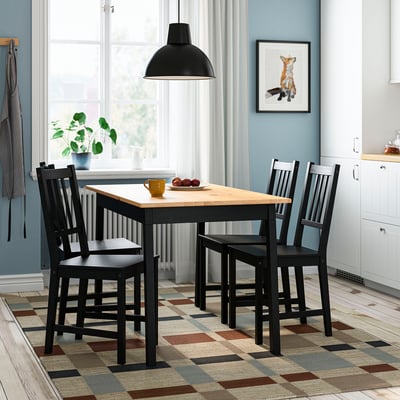 A PINNTORP black dining set with rectangular table and four matching pine chairs, designed to slide under the table for space-saving.