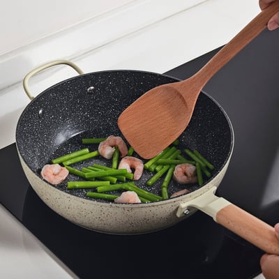 Person cooking shrimp and asparagus in a speckled pan on a stove.