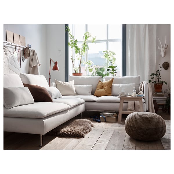 Cosy living room with white l-shaped sofa, colourful pillows, wood floor, and large window. Decorated with plants and a unique lamp.