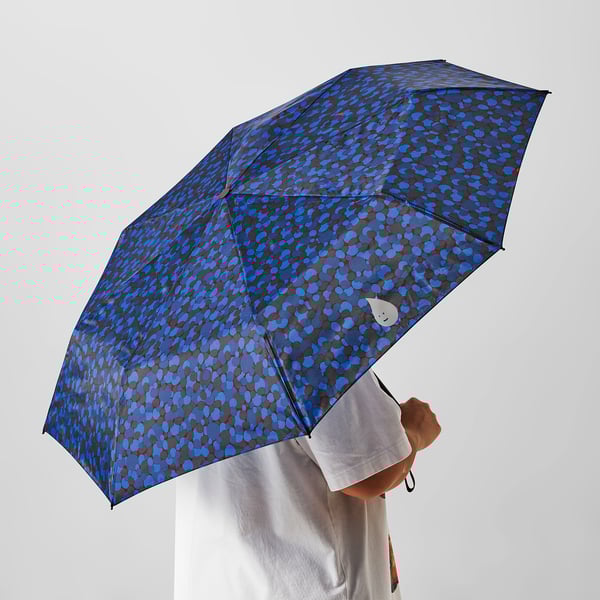 A person holding a blue patterned umbrella with large polka dots over their head.